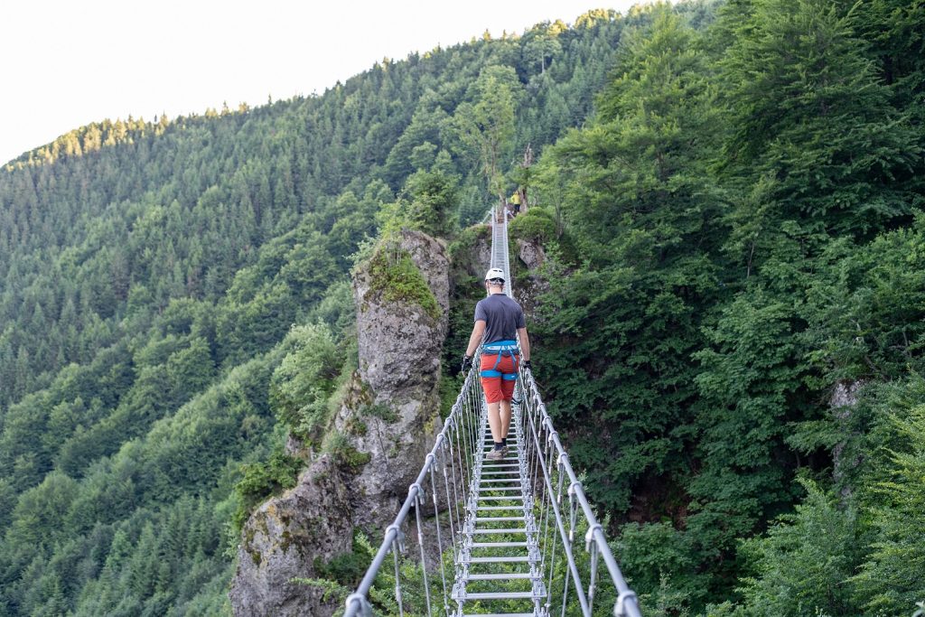 Lezec prechádzajúci po dlhom visutom moste medzi skalnými bralami na Skalke